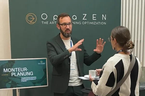Simon Tiffert in conversation at the OptaZEN stand, next to a screen showing the field service scheduling use case